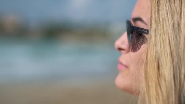 Primer plano de la cara de una chica de cabello rubio en gafas de sol oscuras lamiendo hermosos labios tumbados en una tumbona en la playa en el mar o el océano en verano — Vídeos de Stock