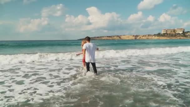 Klädd man och kvinna träder grunt havsvatten i slow motion. Lyckligt par ska bada i vågorna. Fritid för unga familj. Vackra seascape — Stockvideo