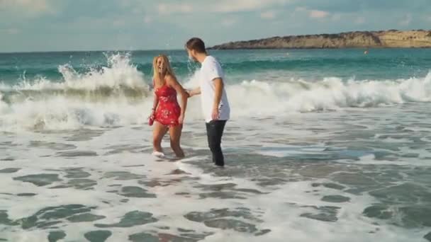 Dressed man and woman standing in shallow sea water. Girl raising her dress a little, panties are visible. Leisure of young family. Beautiful seascape. Image zooms — Stock Video