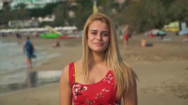 Sahilde uzun sarı saçlı güzel genç kadın portresi. Statik ön plan ve arka plan uzağa sürükleniyor.