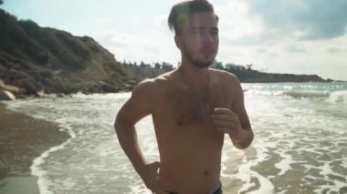 Genç deniz kıyısı sabah koşan adam sakallı. Ağır çekimde deniz kenarında yürüyüş. Sağlıklı bir yaşam tarzı. Yaz plaj