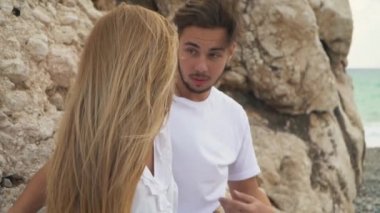 Mutlu çift birbirine bakarak bir kayanın üzerine oturmuş kapatın. Erkek ve kadın beyaz gömlek açık havada sessiz özel yerde vakit