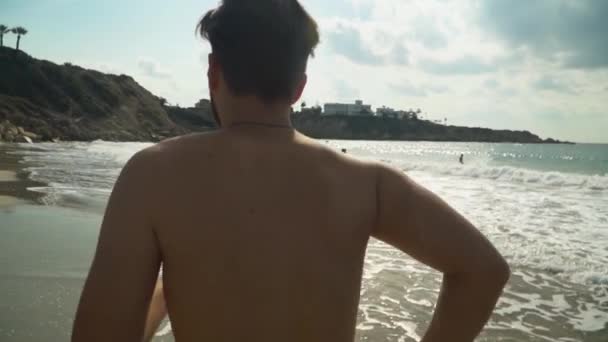 Ung man kör längs havsstranden på morgonen. Jogga nära havet i slow motion. Hälsosam livsstil. Sommar på stranden — Stockvideo