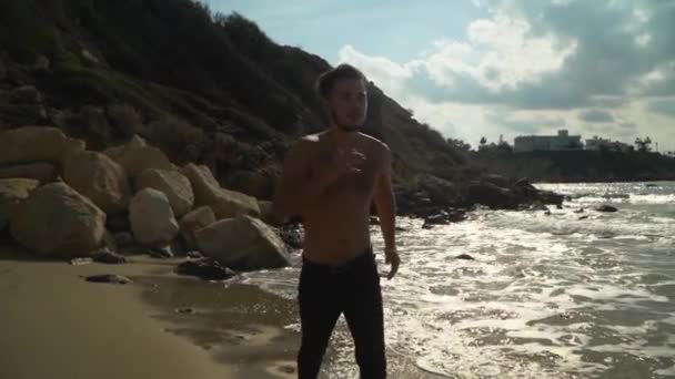 Junger bärtiger Mann, der morgens an der Küste entlang läuft. Joggen am Meer in Zeitlupe. Gesunder Lebensstil. Sommer am Strand — Stockvideo