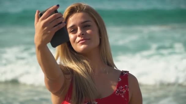 Mooi meisje poseren maakt selfie op de achtergrond van een prachtige zee met de golven op de zomervakantie — Stockvideo