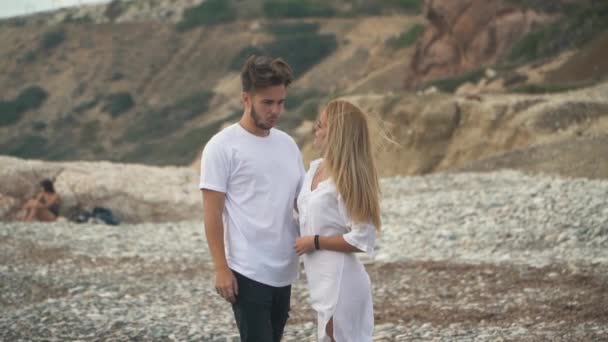 コストの話をスローモーションで岩の海に立っている若いカップル、男と女を抱きしめるお互い優しく、自分の髪がなびきます。若い家族のレジャー — ストック動画