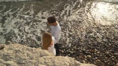 Üstten Görünüm büyük dalgalar, köpük oluşturma ile bir kayalık okyanus kıyısında yürüyen genç sohbet çiftin. Ağır çekim