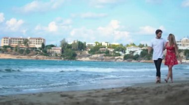 Genç çift birbirleri ile konuşan ve having fun town arka plan üzerinde boş sahilde günbatımı doğru yürüyüş elele