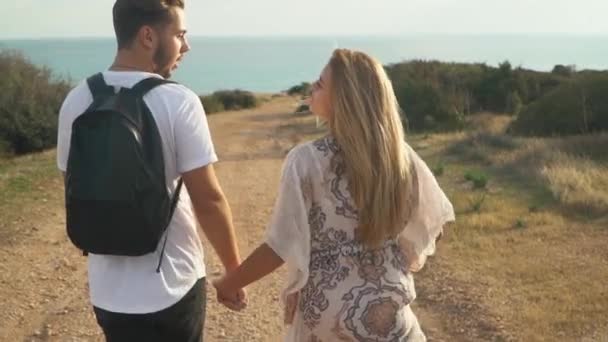 Jeune couple se tenant la main allant sur le rivage de la mer sans fin parlant entre eux et s'amusant. Mouvement lent — Video
