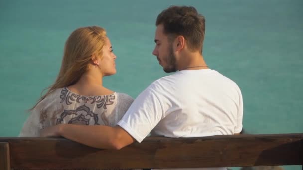 Man och kvinna prata sittande på bänken, havet är i bakgrunden. Lyckligt par umgås utomhus. Fritidsaktiviteter på sommaren — Stockvideo