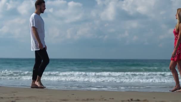 Jonge kerel en een mooi meisje gaan aan elkaar langs de kust, houden de handen en zachtjes glimlachen en kijken elkaar aan hun ogen — Stockvideo