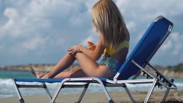 Mädchen liegt auf einer Liege am Strand und benutzt Sonnenbrand-Spray am Körper, um sich nicht in der Sonne zu verbrennen — Stockvideo