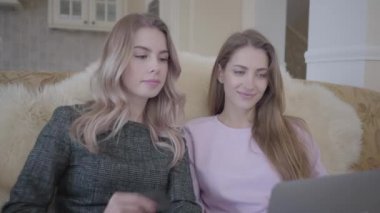 İki genç ve güzel irlfriends oturma odasında kanepede oturan onların dizüstü bilgisayarda Internet üzerinden alışveriş iyi indirimler arıyoruz. Bir kız bir kredi kartı için onun el hazır tutar