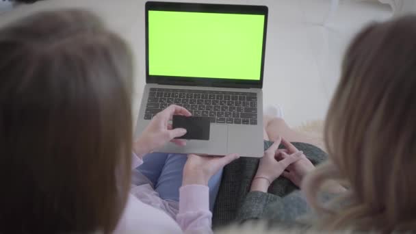 Dwie młode kobiety szukam dobrych rabatów na zakupy, korzystanie z Internetu na komputerze przenośnym z zielonego ekranu siedzi na kanapie w salonie. Jedna dziewczyna daje do innej karty kredytowej. Girlfriends — Wideo stockowe