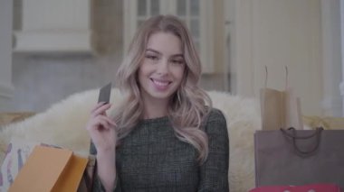 Bir sürü alışveriş torbaları oturma odasında kanepede oturan emin gülümseyen genç ve güzel kadın portresi. Bir kredi kartı tutan başarılı kız. Alışveriş kavramı.