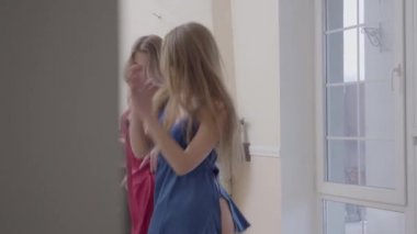 Geniş zeminden tavana uzanan pencere yakınında modern oturma odasında sabah dans iki güzel kadın. Kırmızı ve mavi nighties giyinmiş kız evde eğlenin. Kadın dostluk kavramı