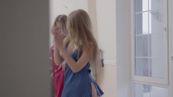 Twee mooie vrouwen dansen in moderne woonkamer in de buurt van groot raam van de vloer tot het plafond in de ochtend. Gekleed in rood en blauw nachtkleding vriendinnen hebben een leuk thuis. Concept van vrouwen vriendschap — Stockvideo