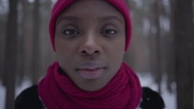 Afro-Amerikan kız kış orman kamera bakıyor ayakta portresi kapatın. Güzel kız açık havada vakit sıcak ceketli. Kamera sola taşır. Gerçek insanlar serisi.