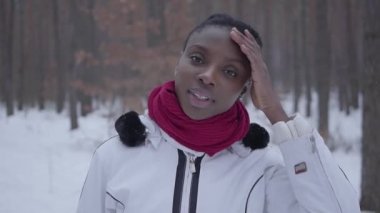 Şirin Afro-Amerikan kız kış orman kamera bakıyor ayakta portresi kapatın. Güzel kız sıcak ceketli eliyle saçlarını düzeltir. Açık Rekreasyon kavramı. Ağır çekim