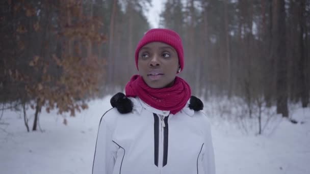 African american girl walking in winter forest looking around, she straightens her scarf. Beautiful girl in warm jacket spending time outdoors. Slow motion shooting — Stock Video