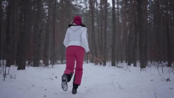 Menina afro-americana correndo pela floresta de inverno. Menina bonita na jaqueta quente vira e olha ao redor, ela está com medo. Mulher é perseguido por perseguidor invisível — Vídeo de Stock