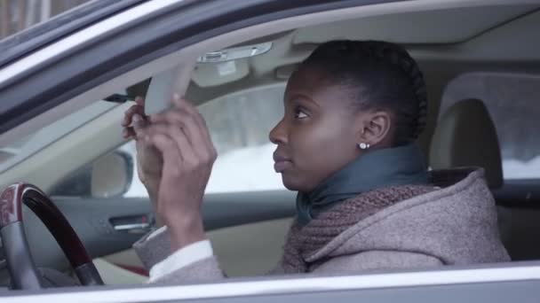 Portrait of self-confident african american woman sitting in the car chewing gum close up. Beautiful woman driving in winter, snowflakes falling outdoors — Stock Video