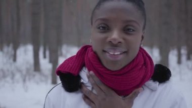 Afro-Amerikan kız kırmızı eşarp ve kış ormanda poz beyaz ceket giyiyor sıcak giyinmiş.