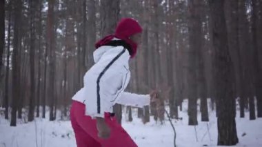 Sıcak giyen bir kırmızı şapka, eşarp ve beyaz ceket karlı ormanda çalışan korkmuş Afro-Amerikan güzel kadın giyinmiş. Kız sürekli geri çalışan takipçisi uzak görünüyor. Ağır çekim.