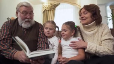Komuta sizde ve iki küçük kız arasında onları ile modern oturma odasında deri kanepede oturan kadın. Olgun adam onun granddaughters için kitap okuma. Mutlu aile eğlence
