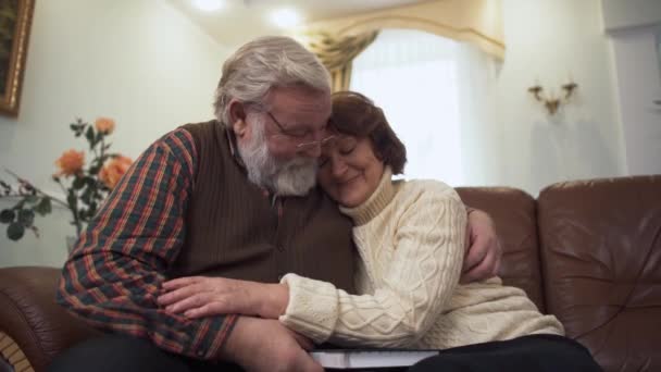 Glückliches älteres Paar, das auf dem Sofa im modernen Wohnzimmer zu Hause sitzt. Ältere Männer und Frauen kuscheln miteinander. Freizeit der Seniorenfamilie — Stockvideo