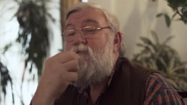 Üst düzey sakallı adam evde, sonra oturup gösterir büyük parmak kiraz yiyor. Olgun erkek sağlıklı yaşam tarzı olur. Karanfiller arka planda vardır