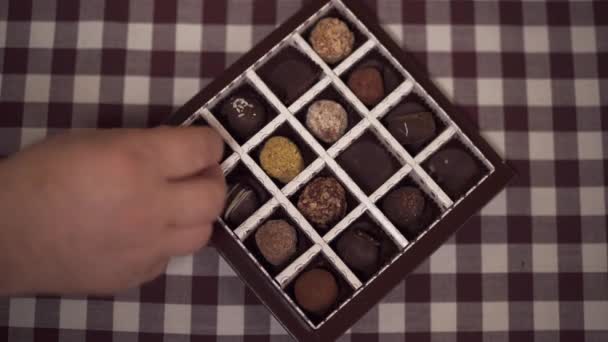 Manos de adultos y niños poniendo dulces de nuevo en la caja. Los niños y abuelos comen chocolate en casa. Primer plano. . — Vídeos de Stock