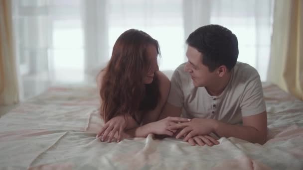 Szczęśliwa para rozmów i pocałunek, leżącego w komfortowe łóżko rano z bliska. Mężczyzna i Kobieta, trzymając się za ręce. Szczęśliwi kochankowie razem — Wideo stockowe