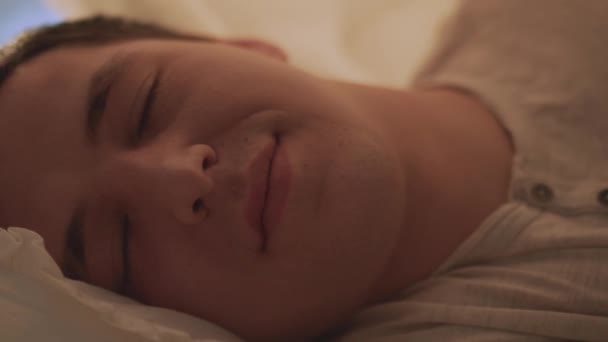 Лицо молодого человека с закрытыми глазами, парень спит в постели — стоковое видео
