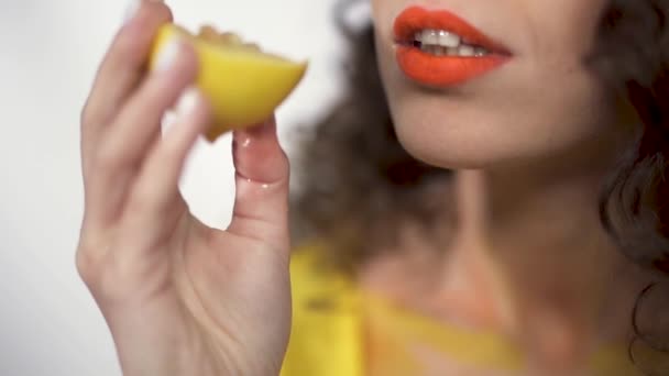 Vista de cerca de los labios regordetes con lápiz labial naranja brillante que muerde el pedazo agrio de limón con placer. Movimiento lento — Vídeo de stock