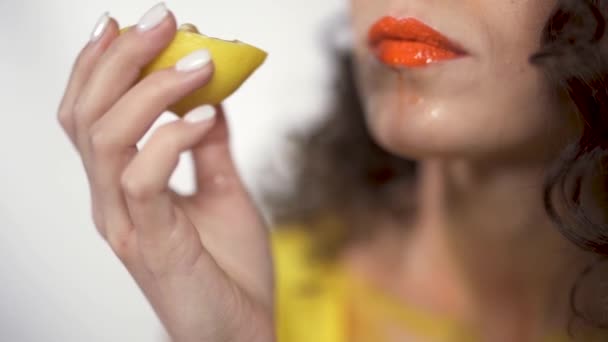 Nahaufnahme von feuchten dicken Lippen mit leuchtend orangefarbenem Lippenstift, der genüsslich in saure Zitronen beißt. Zeitlupe — Stockvideo