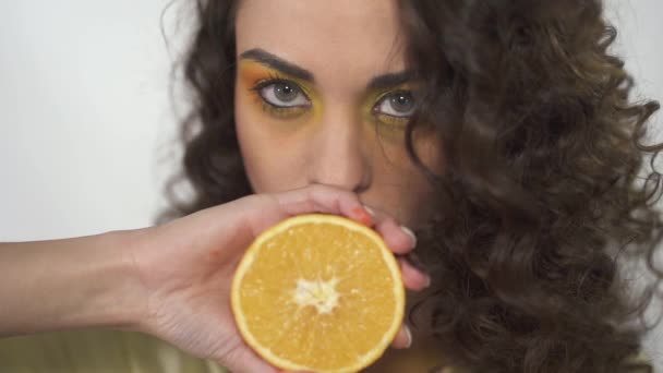 抬起大眼睛可爱的女孩 她的嘴唇附近拿着一个橘子 挤压创造流动的果汁的肖像 慢动作 — 图库视频影像