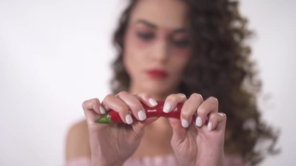 Ritratto di una graziosa ragazza riccia sorridente che tiene in mano un peperoncino rosso e lo spezza in due parti. Rallentatore . — Video Stock