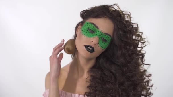 Retrato de hermosa chica rizada con maquillaje creativo conducir kiwi maduro a lo largo de los contornos de la cara y el cuerpo — Vídeo de stock