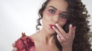 Yarım bir sulu nar tutarak ve parmaklarını yalama gülümseyen genç ve güzel kıvırcık kız portresi.