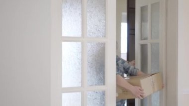 Neşeli erkek ve kadın gündelik elbise eller kutularına ile onların yeni ev için gel. Evli çift yeni bir ev taşır. Gençler kutuları yere koy ve gülümseyen etrafına bak