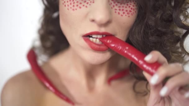 Porträtt av leende ganska ung curly flicka bita liten röd het chili paprika, när två andra är i hennes axlar. — Stockvideo