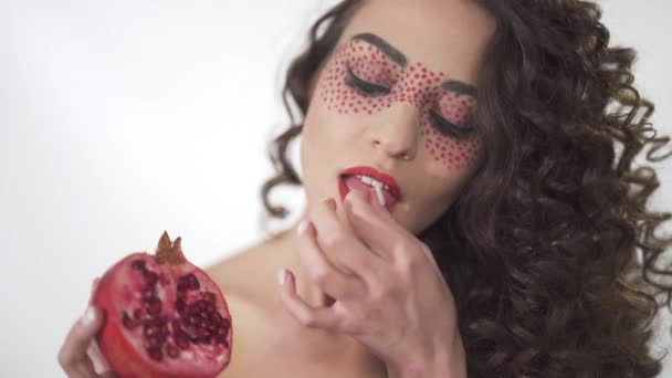 Portrait of nice laughing young curly girl holding in hand and eating pomegranate with smile and fun — Stock Video