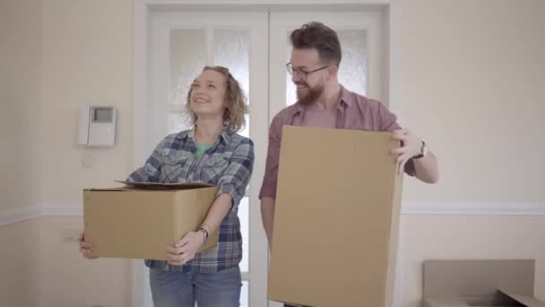 Heureux homme et femme en robe décontractée avec des boîtes dans les mains debout dans la pièce en regardant autour de près. Un couple marié emménage dans une nouvelle maison. Les gens mettent des boîtes les uns sur les autres, les femmes soupirent de soulagement — Video