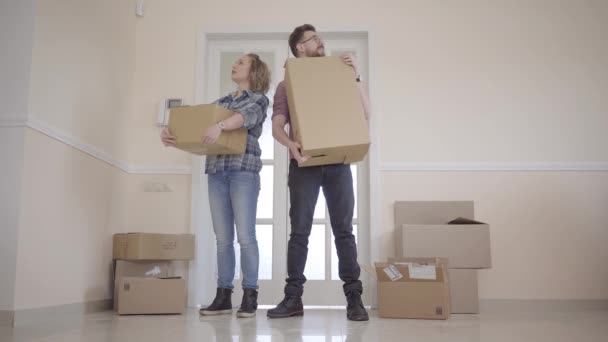 Um jovem casal a mudar-se para uma nova casa. Um casal está na porta segurando caixas em suas mãos. Belo casal estão se beijando e estão inspecionando o apartamento . — Vídeo de Stock