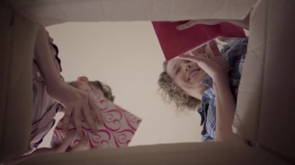 Hombre barbudo con gafas y mujer sonriente inclinarse sobre la caja y pasar páginas de libros que se tomó de ella. La familia feliz desempaca las cosas después de mudarse a casa nueva. Vista de abajo. Disparos desde la caja — Vídeo de stock