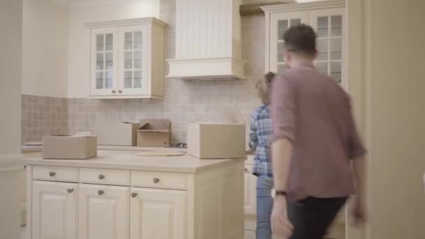 Glædelig ung familie fjoller rundt i køkkenet i deres nye hjem. Et lykkeligt par flytter til en ny lejlighed. Mand jagter sin kone i køkkenet . – Stock-video