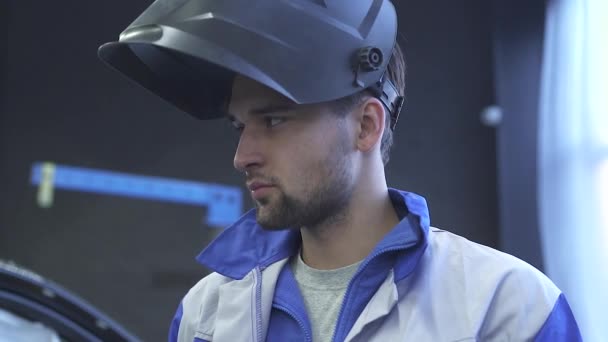 Retrato de jovem especialista mecânico de automóveis em soldagem capacete no fundo do serviço de carro moderno. Movimento lento — Vídeo de Stock