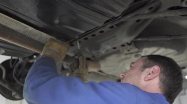 Otomatik mekanik bir anahtar ile arabanın altına ayakta ve servis istasyonunda civata sıkma mavi üniformalı deneyimli.