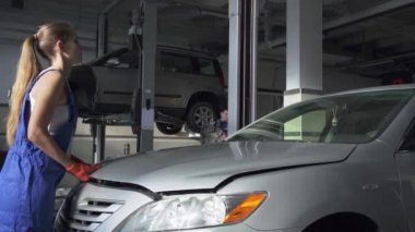 Kadın genç otomatik uzman onarımı veya araba servisi yapıyor için arabanın kaputu açmak. Araba Servisi, tamir, bakım ve insan kavramı - atölyesinde çalışan makinist kadın.